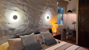 Een slaapkamer met een groot bed, een nachtkastje met een lamp, een raam met uitzicht op groen, en een plafondlamp.