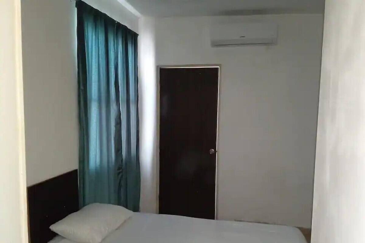 A simple hotel room with a single bed, a dark door, and a window with blue curtains.