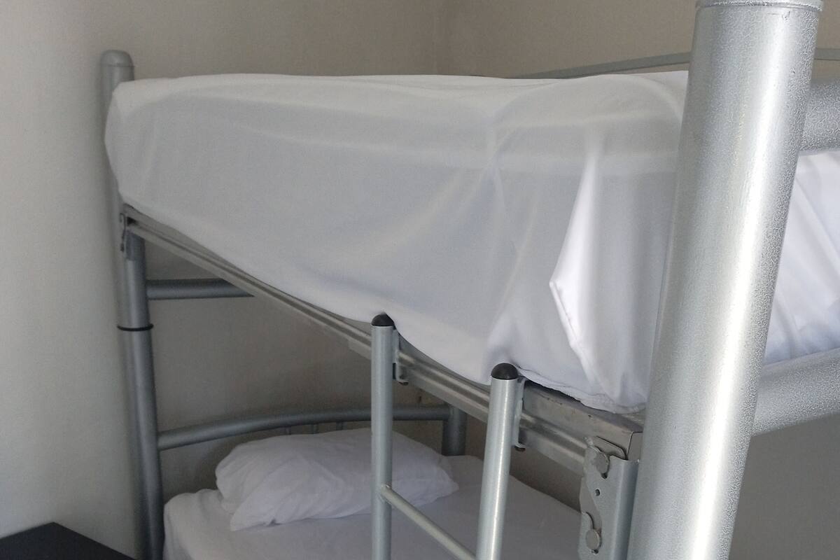 A bunk bed with metal railings, a white mattress, and a black nightstand with drawers.