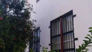 A building with two windows, a small tree with red fruits, and a concrete pathway. - Santa Rosa 4Rest (Apodaca)