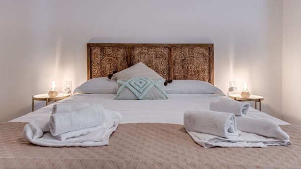 A neatly made bed with a quilted headboard, two bedside tables with lamps, and folded towels on the bed. - Boho - Sweet Dreams in Florence (Firenze)