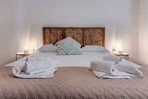 Una cama bien hecha con un cabecero acolchado, dos mesitas de noche con lámparas y toallas dobladas sobre la cama.