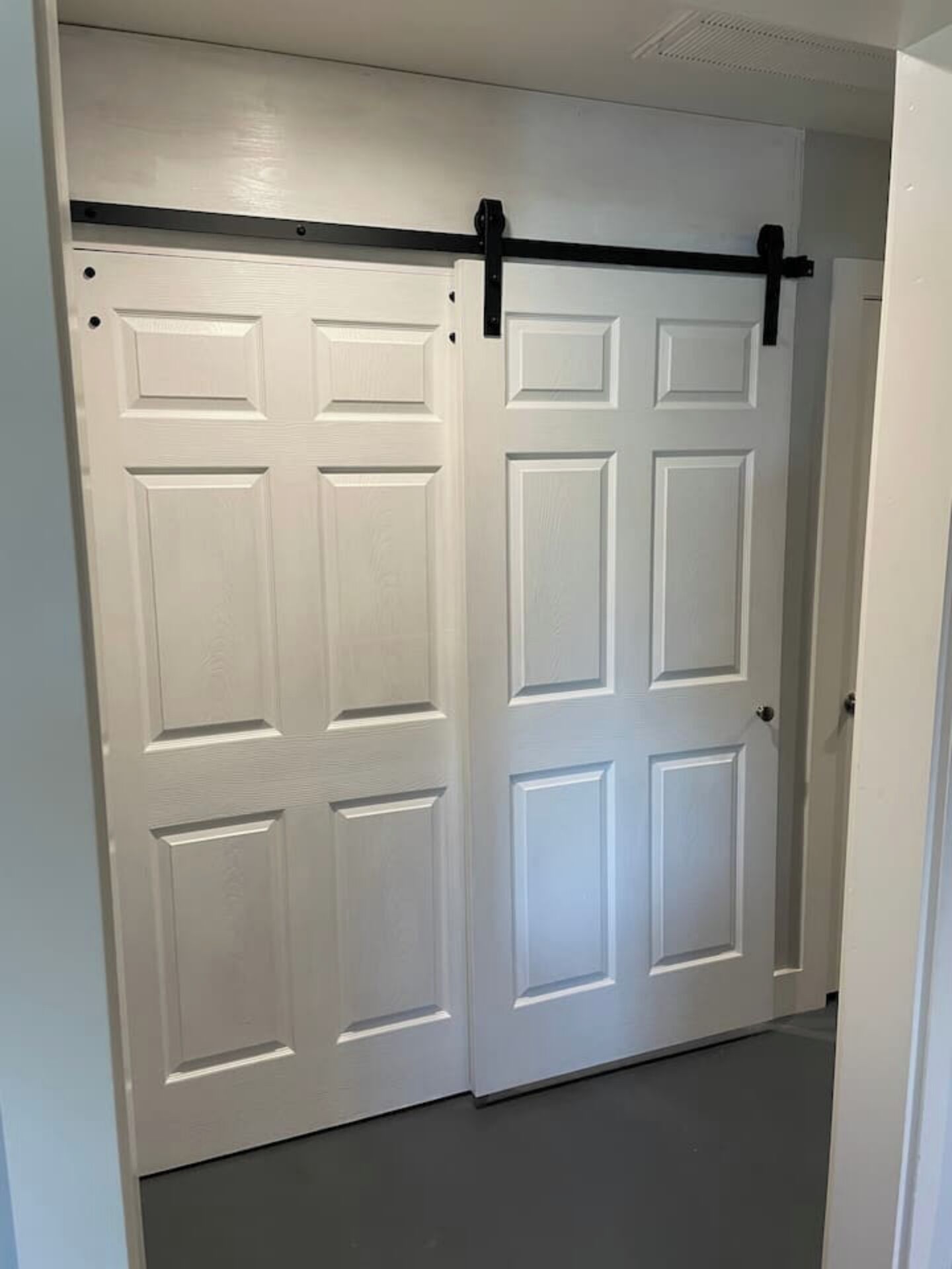 Une paire de portes doubles blanches, surmontée d’une barre horizontale noire, probablement conçue pour permettre une ouverture coulissante.