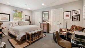 A bedroom with a large bed, a desk, a chair, a dresser, and a mirror.