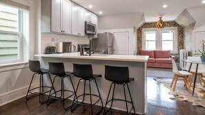 Una cocina moderna con una isla central, taburetes de bar, zona de comedor con un sofá rosa y pared con diseño.