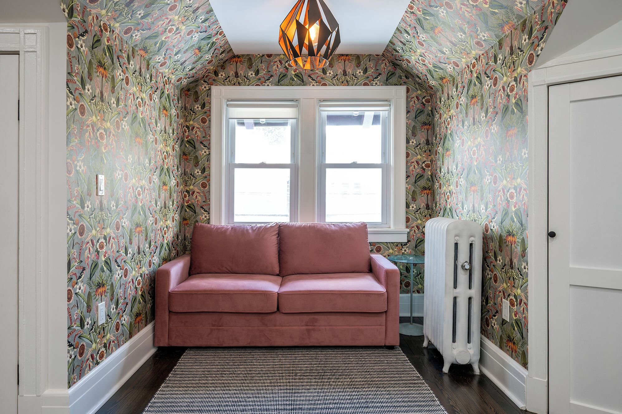 A room with floral wallpaper, a pink sofa, a zebra-patterned rug, and a radiator.
