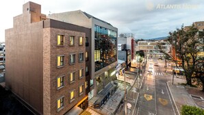 A modern building with a mix of brick and glass facades, a visible entrance, and a street view with cars and a pedestrian crossing. - Atlantis Home Zona T (Bogotá)