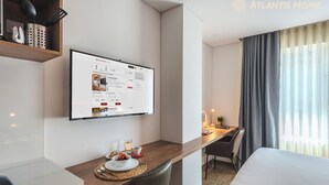 A modern hotel room with a wooden desk, a bed, and a large window with curtains. - Atlantis Home Zona T (Bogotá)