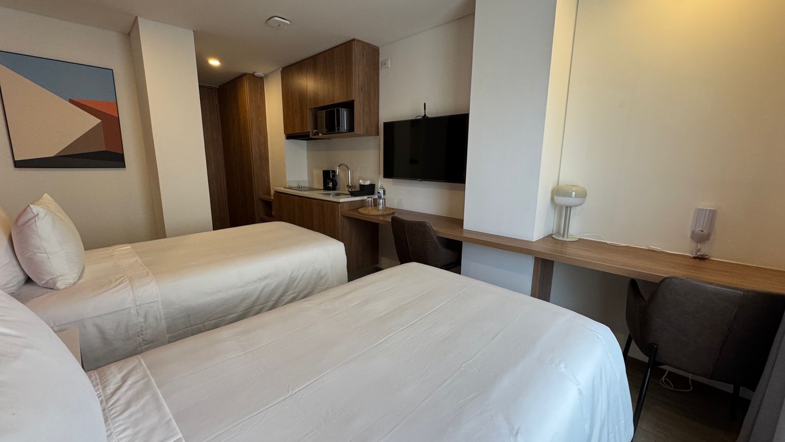 A hotel room with two beds, a desk, a chair, a TV, and a microwave.