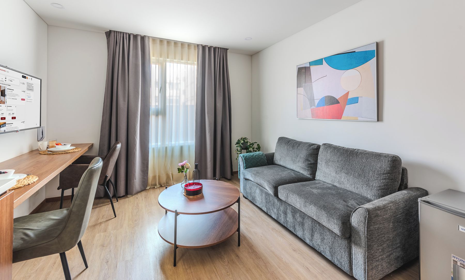 A modern living room with a grey sofa, a round coffee table, and a dining area with a wooden table and chairs.