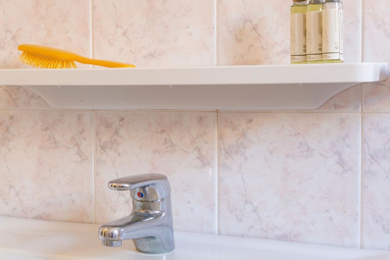 Un baño con un estante blanco que sostiene un cepillo amarillo y tres botellas.