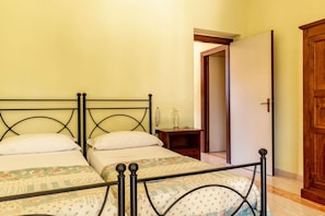 A bedroom with two single beds, a wooden nightstand, and a door leading to another room.
