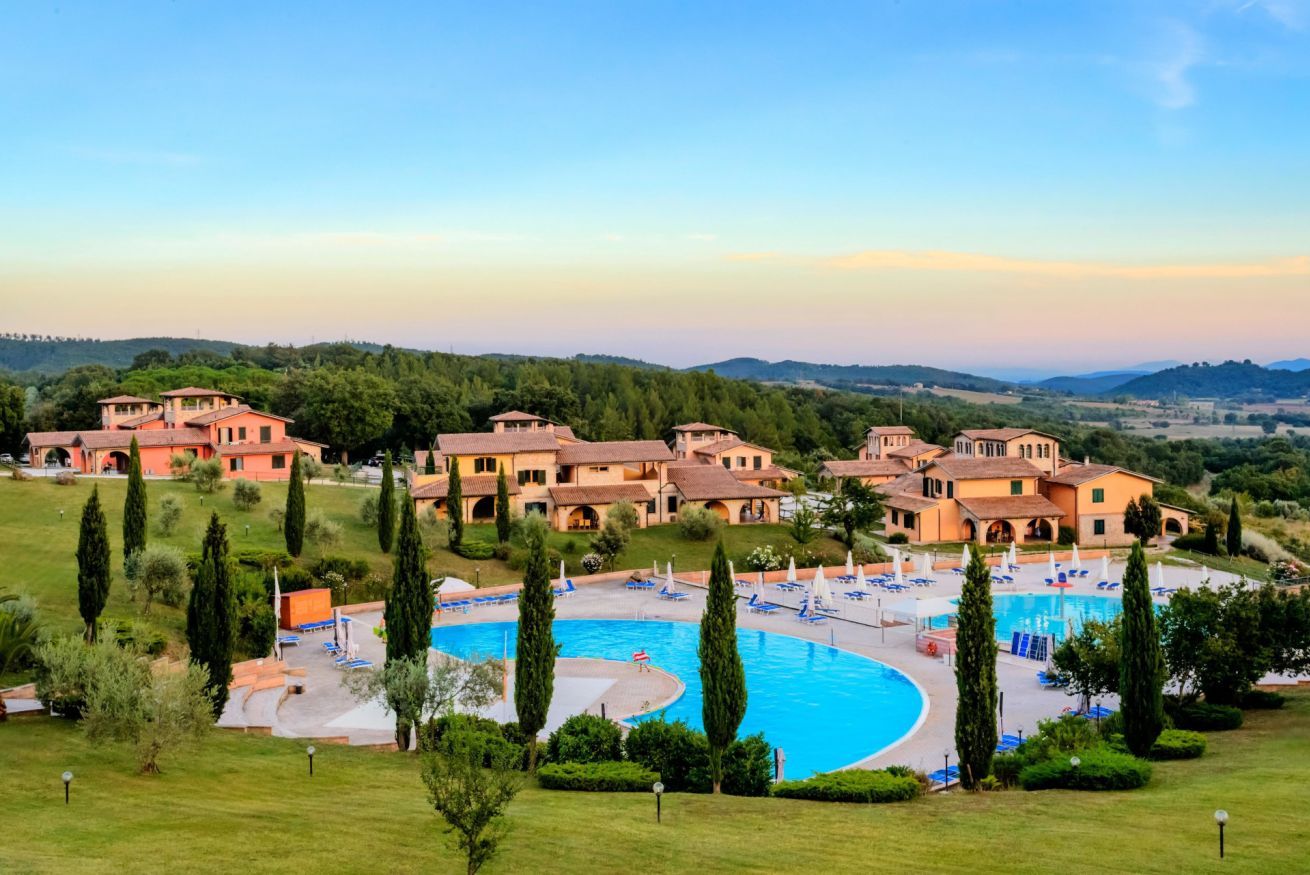 A resort with multiple buildings, a central swimming pool, and a well-maintained lawn.