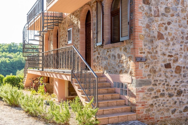 A stone building with a balcony, a staircase, and a door.
