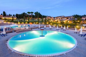 A circular pool with lounge chairs and umbrellas, surrounded by buildings and trees.