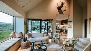 A spacious living area with a large window, a fireplace, and a dining area with a view of the outdoors. - Ranger's Retreat - Secluded - Sleeps 4 (Lake Hawea)