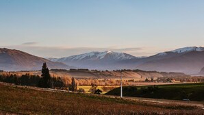 A rural landscape with rolling hills, a clear sky, and distant snow-capped mountains. - Ranger's Retreat - Secluded - Sleeps 4 (Lake Hawea)