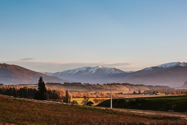 A rural landscape with rolling hills, a clear sky, and distant snow-capped mountains.