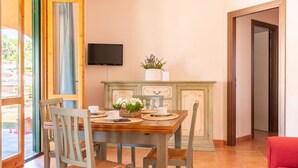 Uma área de refeições com uma mesa de madeira posta para dois, rodeada por cadeiras. Uma televisão está fixada na parede acima da mesa.