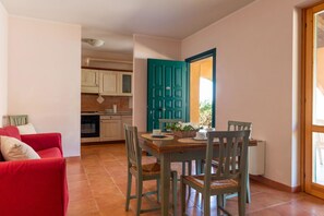 Un coin repas avec une table et des chaises en bois, un canapé rouge et une porte de couleur turquoise.