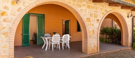 A stone building with two arches, a table with chairs, and a basket on the ground.