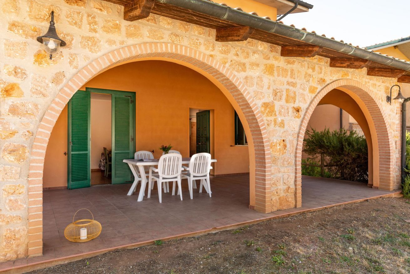 A stone building with two arches, a table with chairs, and a basket on the ground.