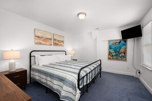Ein Schlafzimmer mit Bett, Nachttischen, Kunstwerken, einem Fernseher und einem Fenster.