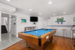 Ein Billardtisch mit blauer Spielvliesdecke, einem Holzrahmen und einer weißen Wand, an der ein Fernseher und eine grüne Krabbendekoration befestigt sind.