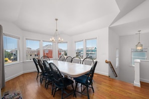 A dining room with a large table and chairs, large windows, and a chandelier.