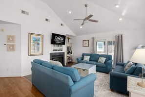 A living room with a fireplace, blue sofas, a flat-screen TV, and a ceiling fan.