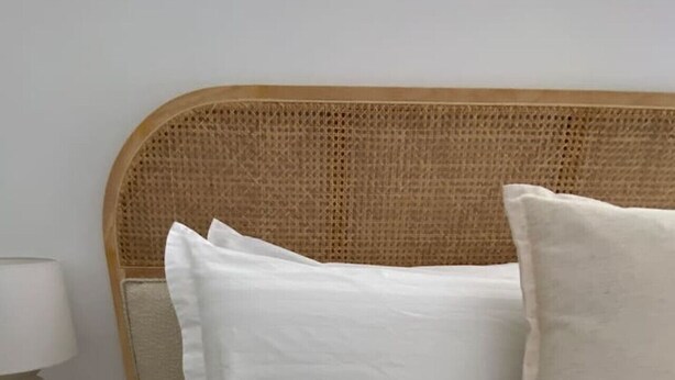 A bed with white bedding and a woven headboard.
