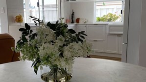A kitchen with white cabinets, a marble countertop, and a vase with white flowers.