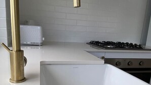 A kitchen with a white countertop, a stainless steel sink, a gas stove, and white cabinets.