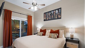A bedroom with a large bed, two bedside tables, a ceiling fan, and a cityscape artwork on the wall. - Escape to Reames Dream BnB: Lakefront bliss with sand volleyball awaits! (Austin)