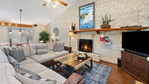 Una sala de estar con chimenea de piedra, un televisor grande y un ventilador de techo.