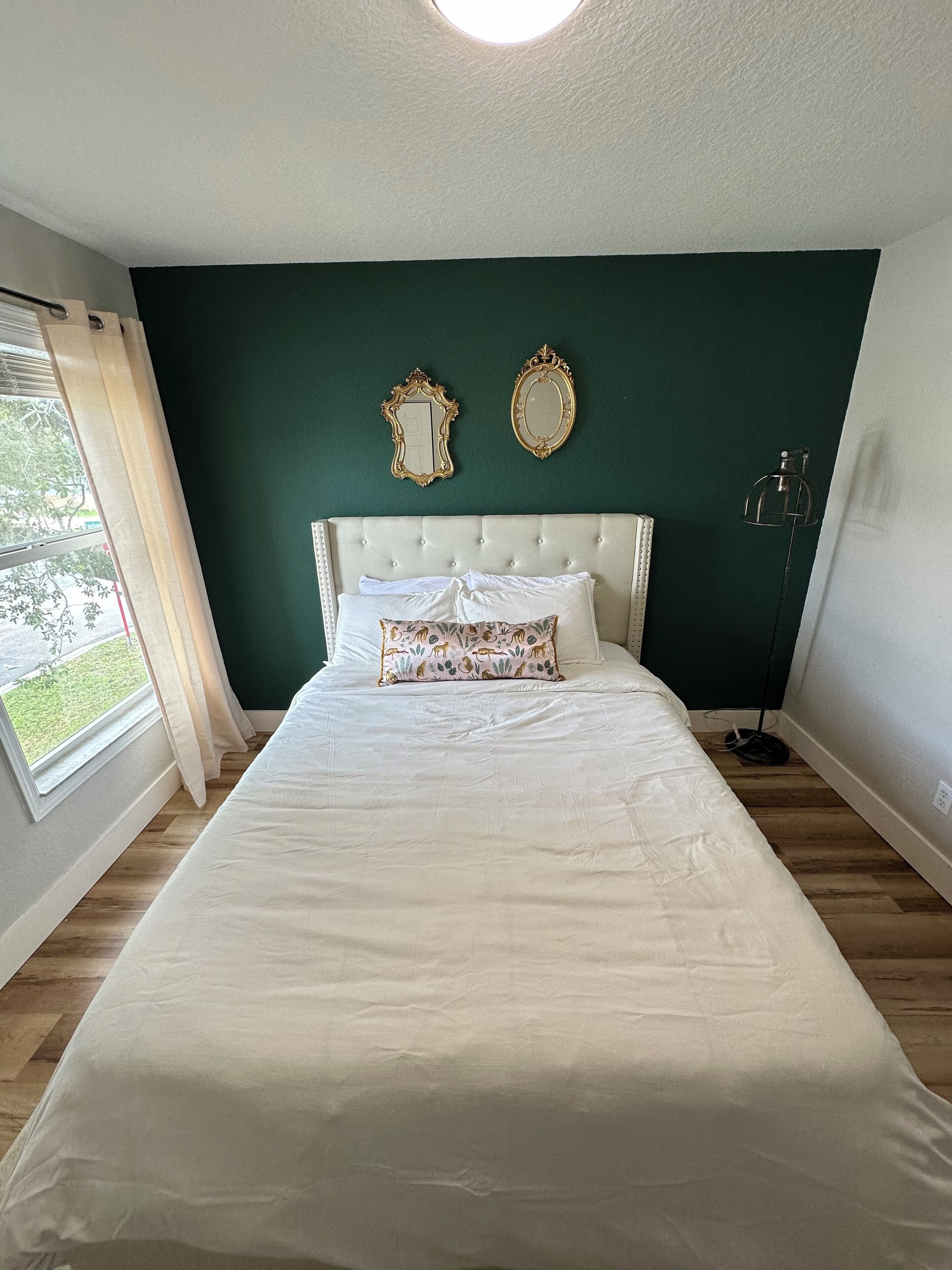 A bedroom with a large bed, a window with curtains, and two wall mirrors.