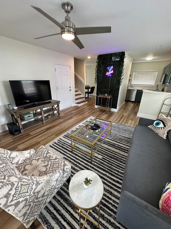 A modern living room with a flat-screen TV, a ceiling fan, a coffee table, and a sofa.