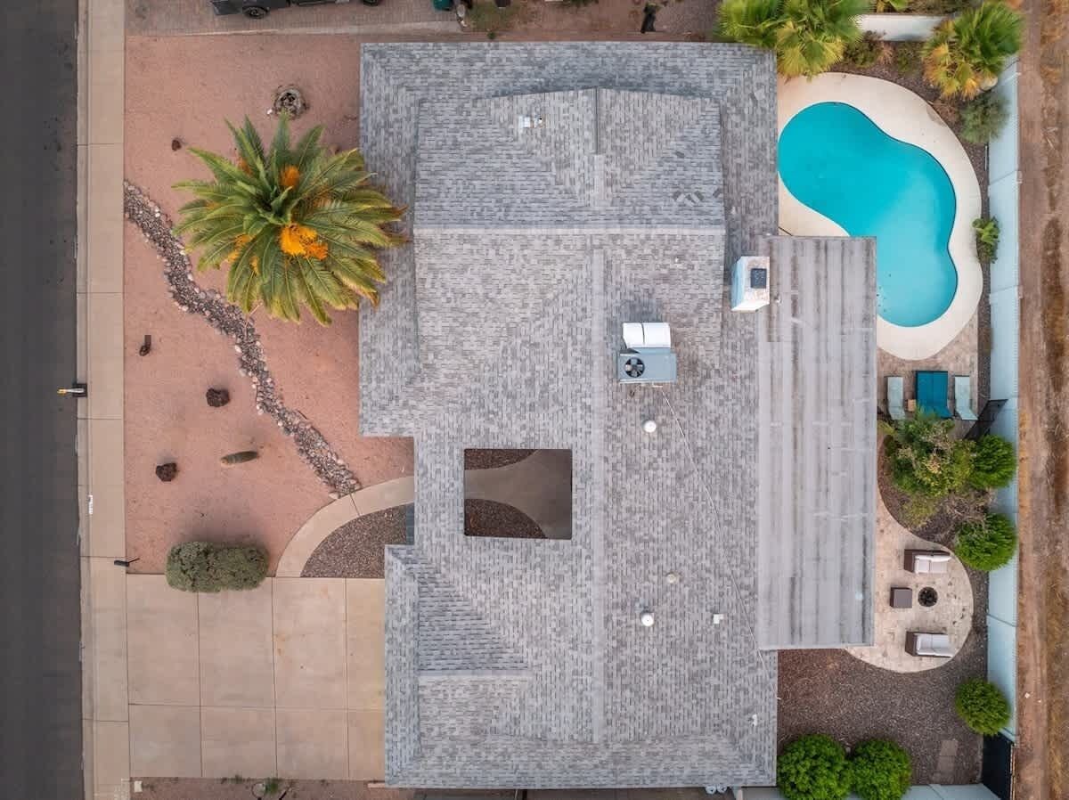 An aerial view of a property with a swimming pool, patio area, and a small garden with a palm tree.