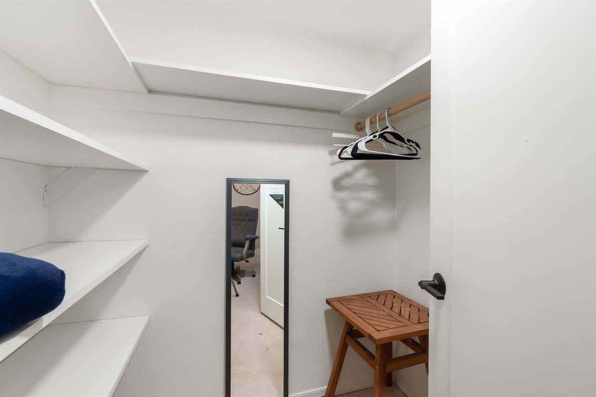 Une petite pièce avec une porte de placard miroir, une chaise en bois et une couverture de lit bleue.