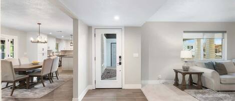 Una sala de estar moderna con un sofá, un comedor con mesa y sillas, y una cocina visible a través de una puerta abierta.