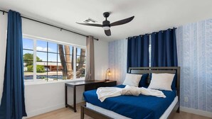 Un dormitori modern amb un llit gran, una taula de treball i un ventilador de sostre.
