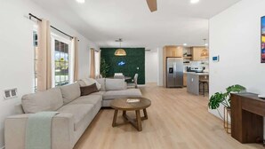 Un saló modern amb un sofà, una taula de centre i una paret verda. Hi ha una zona de cuina amb un frigorífic i una taula de menjador.
