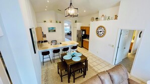 Una cocina moderna con una isla central, un comedor con mesa y sillas, y una sala de estar con un sofá marrón.