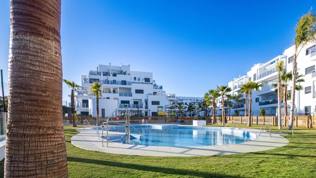 Un hôtel moderne doté d’une piscine, de palmiers et surplombant un ciel d’un bleu limpide.