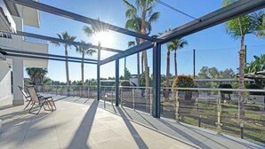 A sunlit balcony with a clear view of palm trees and a road.