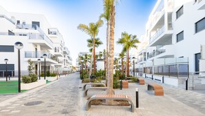 Une promenade urbaine moderne, agrémentée de bancs, de palmiers et de bâtiments blancs dotés de balcons.