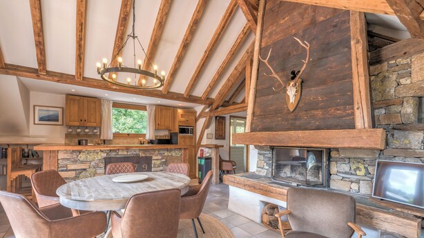 A rustic interior with a stone fireplace, wooden beams, and a dining area with chairs.