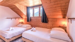 A room with two wooden beds, a sloped ceiling, and a window with curtains.