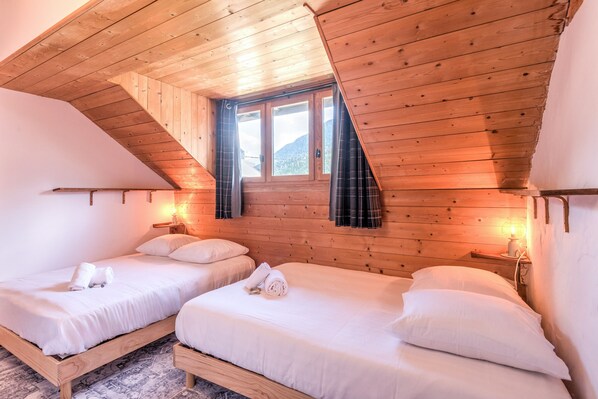 A room with two wooden beds, a sloped ceiling, and a window with curtains.
