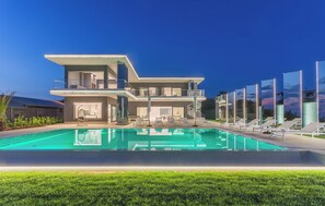 Ett modernt hus i två våningar med en swimmingpool, en uteplats och utsikt över solnedgången.